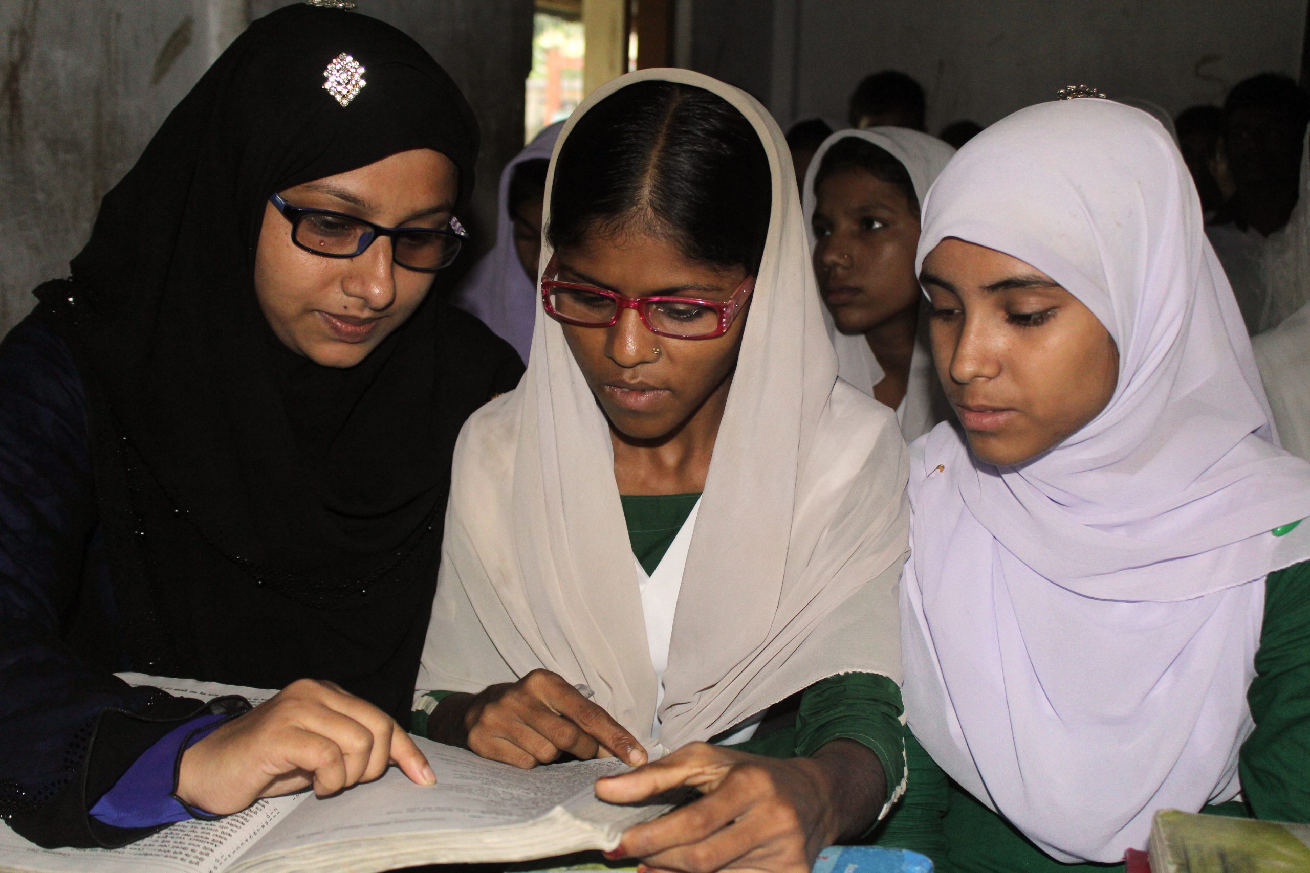 A teacher sitting and reading with two young women A teacher sitting and reading with two young women