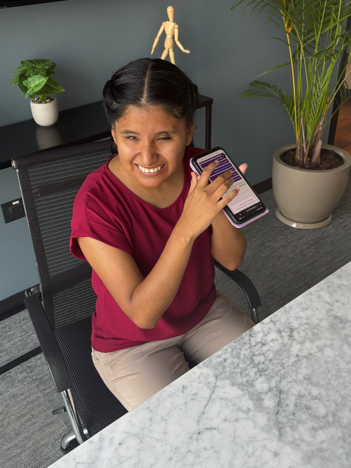 Milagro sat at a desk listening to a resource on the Hub using the Talkback app on her mobile phone.
